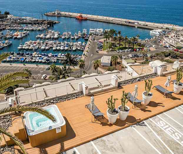 Utsikt över en marina med båtar samt en terrass med jacuzzi och solstolar. (AI-genererad text)