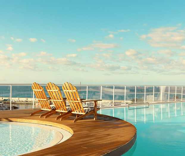 Tre trästolar vid kanten av en pool med en utsikt över havet. (AI-genererad text)