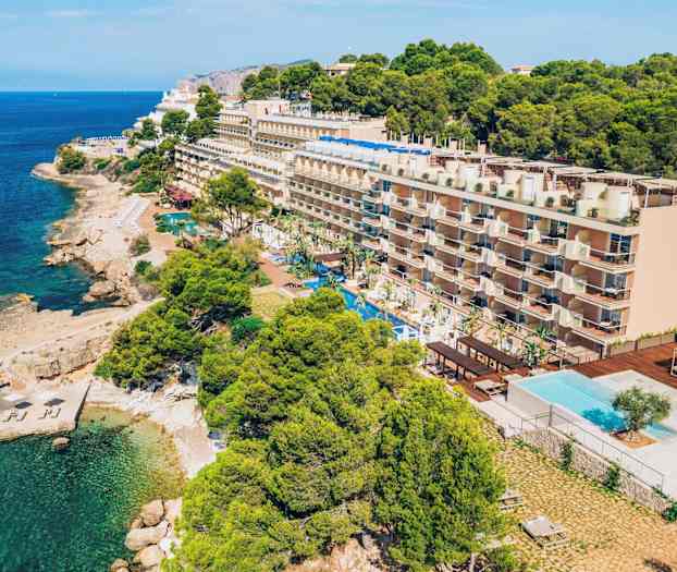 Fyrvåningshotell vid kusten med en swimmingpool framför och omgivande grönska. (AI-genererad text)