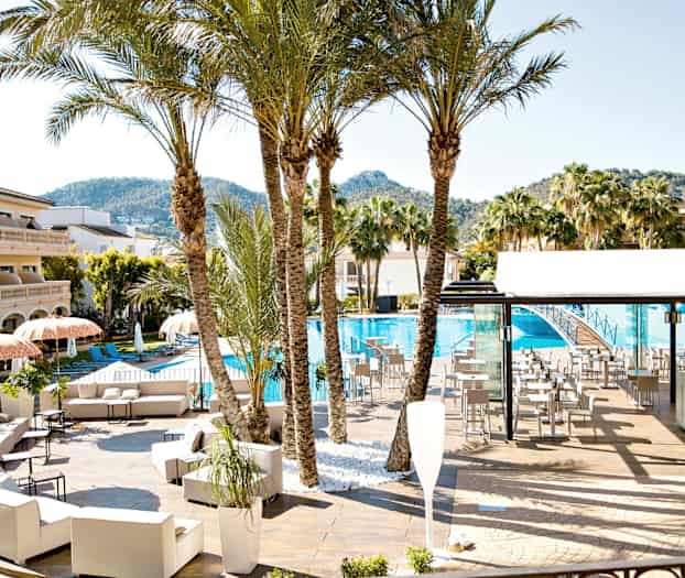 En poolområde med solstolar, parasoller, palmer och en byggnad i bakgrunden. (AI-genererad text)