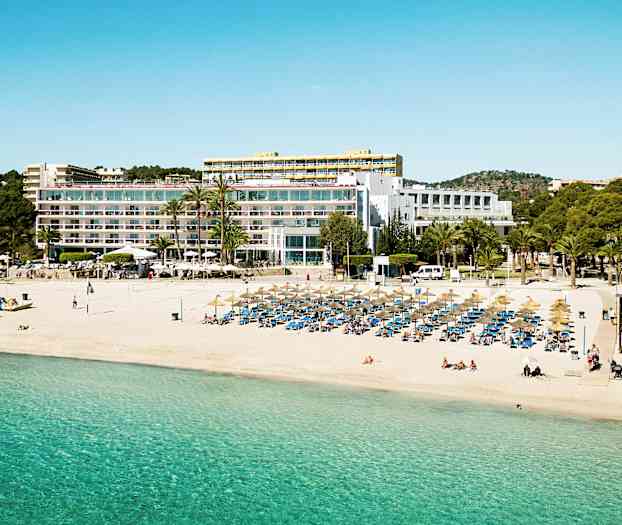 En strand med parasoller och solstolar, framför en stor byggnad med balkonger. (AI-genererad text)