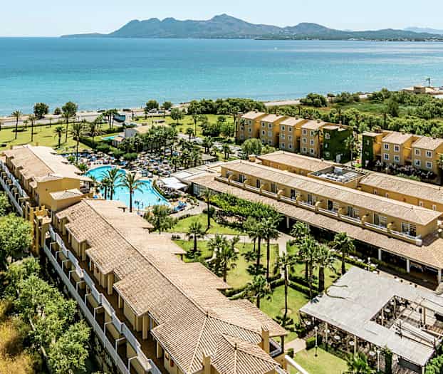 Flygfoto av ett semesterkomplex vid havet med pool, grönområden och flerbostadshus. (AI-genererad text)