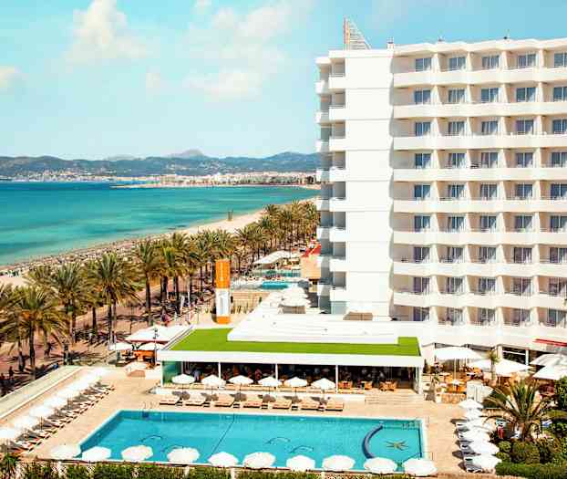 Hotell vid stranden med pool och solstolar, hav i bakgrunden. (AI-genererad text)