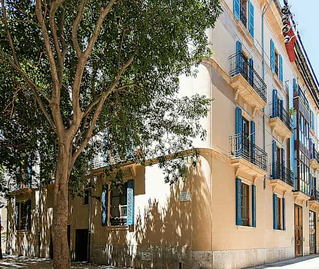 En byggnad med flera balkonger och blå fönsterluckor. (AI-genererad text)