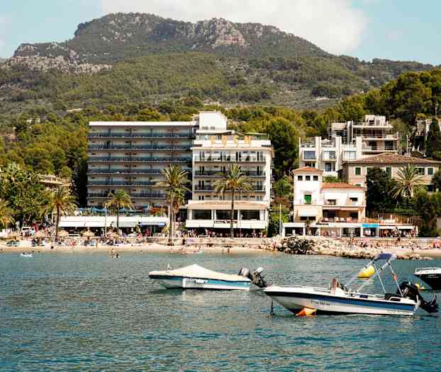 Foto av en kuststad med hotell, strand och båtar vid vattnet. (AI-genererad text)