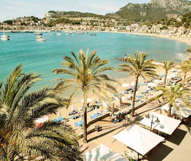 Strand med palmer och solstolar. Vacker vy över havet och närliggande byggnader. (AI-genererad text)