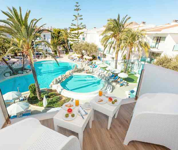 Vy från terrass mot poolområde med solstolar, palmer och frukostbord. (AI-genererad text)