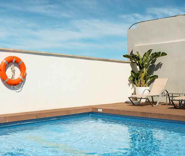 En utomhuspool med två solstolar och en orange livboj hängande på en vit vägg. (AI-genererad text)