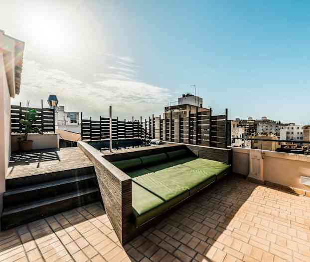 En takterrass med en grön sittplats och utsikt över omgivande byggnader. (AI-genererad text)