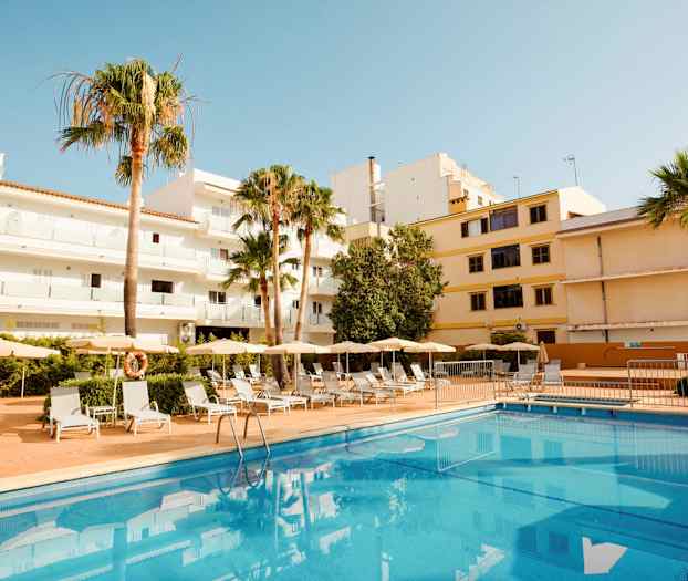 Exteriör av hotell med pool och solstolar, omgiven av byggnader och palmer. (AI-genererad text)