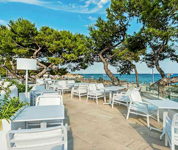 Uteservering med vita möbler och utsikt över havet och stranden. (AI-genererad text)