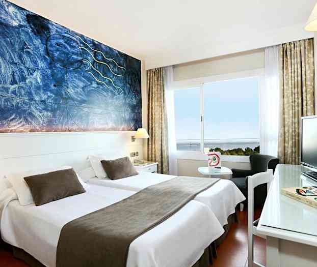 Ett hotellrum med två enkelsängar som har vita sängkläder och bruna överkast, en konstnärlig målning på väggen och ett fönster med utsikt över havet. (AI-genererad text)