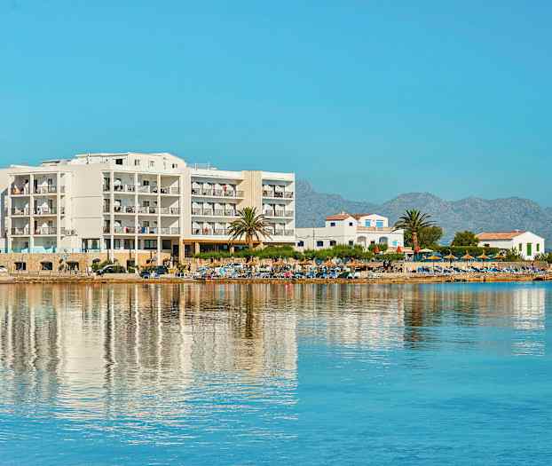 Bild av ett hotell vid stranden med hav och berg i bakgrunden. (AI-genererad text)