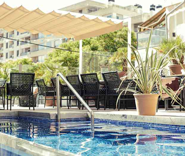 En sittgrupp med svarta möbler vid sidan av en pool med blått kakel, omgiven av krukväxter. (AI-genererad text)