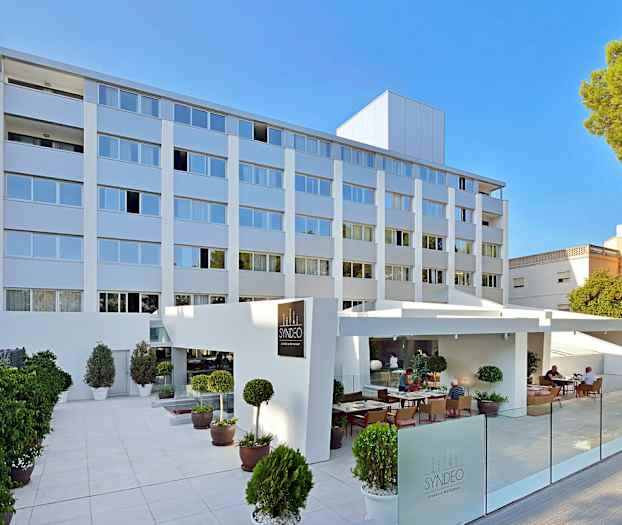 Foto av en modern hotellbyggnad i flera våningar med en uteservering och växter utanför. (AI-genererad text)