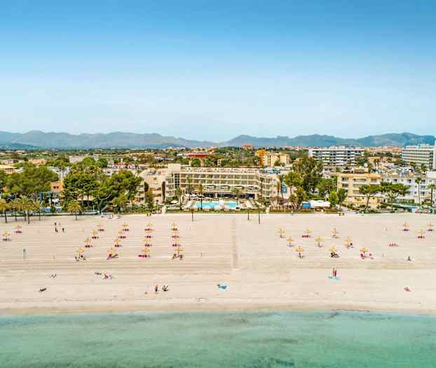 Strand med solsängar och parasoller, hotell samt stadssiluett i bakgrunden. (AI-genererad text)