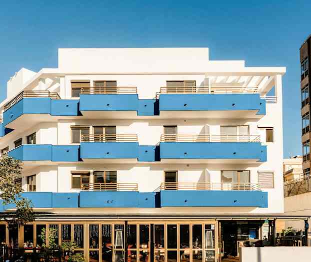 Ett flerfamiljshus med vita väggar och blå balkonger, samt en restaurang på bottenvåningen. (AI-genererad text)