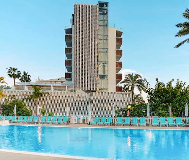 En byggnad med en pool framför samt palmer och solsängar. (AI-genererad text)