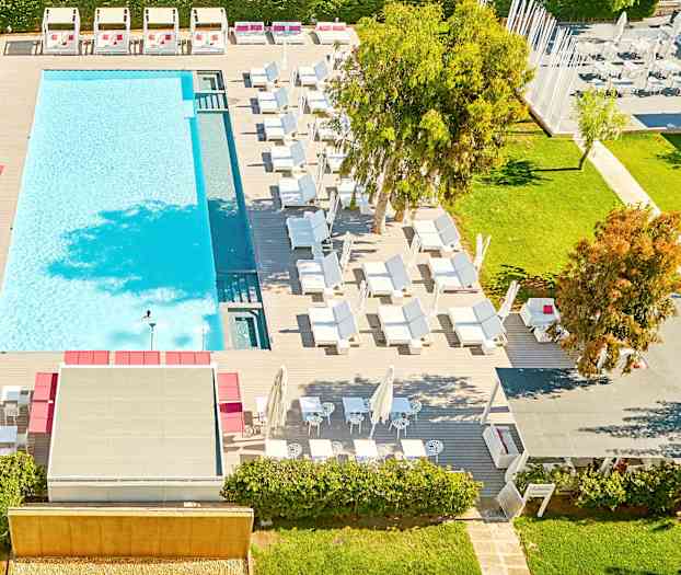 Vy från ovan av en utomhuspool omgiven av solstolar och grönska. (AI-genererad text)