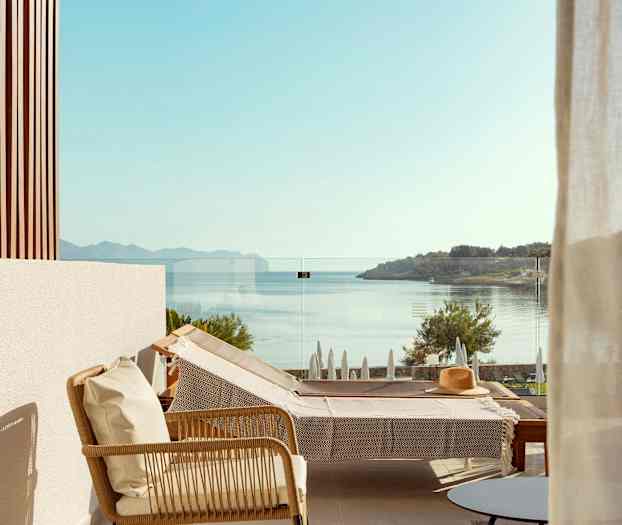 Utsikt från en terrass med en solstol och glasräcke, havet och landskapet syns i bakgrunden. (AI-genererad text)