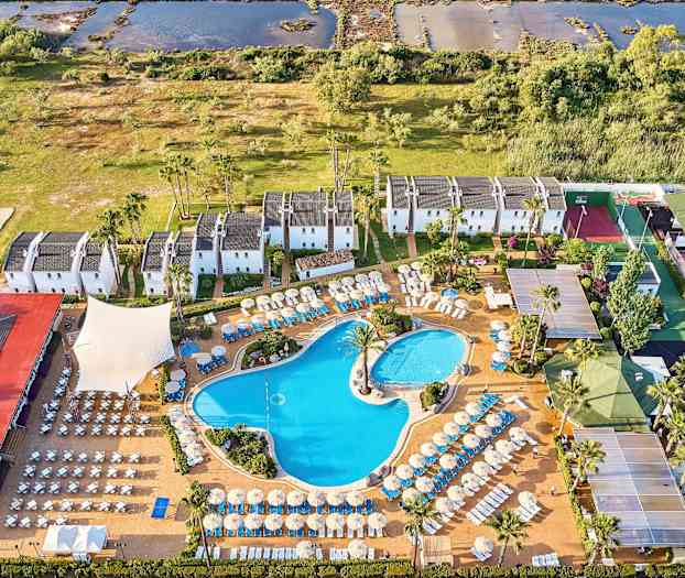 Flygvy över hotellområde med pooler, solstolar och vitmålade byggnader omgivet av grönska. (AI-genererad text)