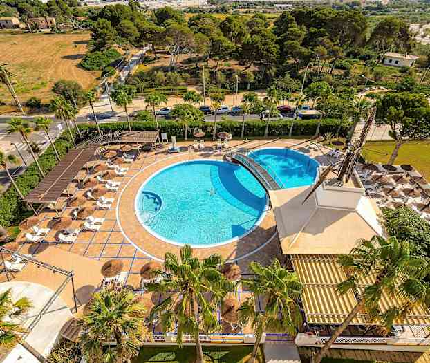 Flygbild av ett utomhusområde med två pooler, solstolar och parasoller, omgiven av grönska. (AI-genererad text)