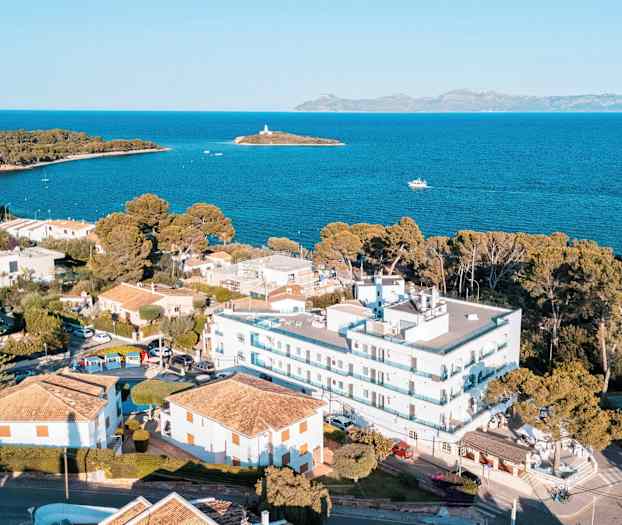 Flygfoto över ett kustnära område med byggnader, strandnära hus och havsutsikt med en liten ö i bakgrunden. (AI-genererad text)