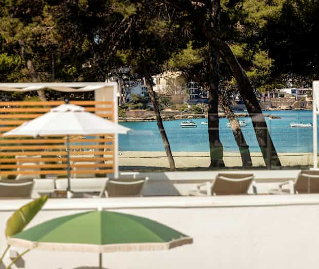 Bild av strand och hav som syns genom trädklyftor, med solstolar och parasoller i förgrunden. (AI-genererad text)