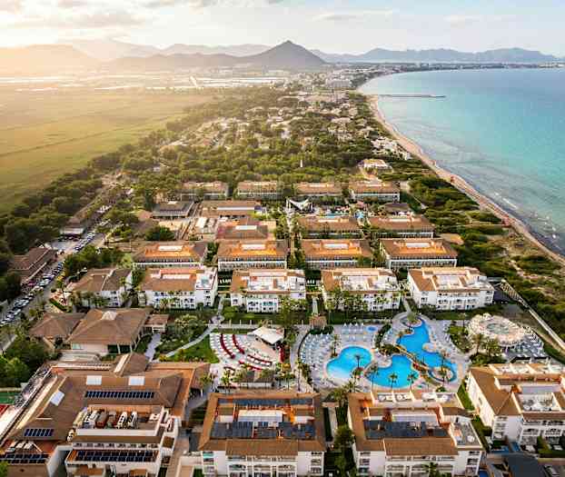 Flygbild av en turistort med hotell och pool vid kusten. (AI-genererad text)