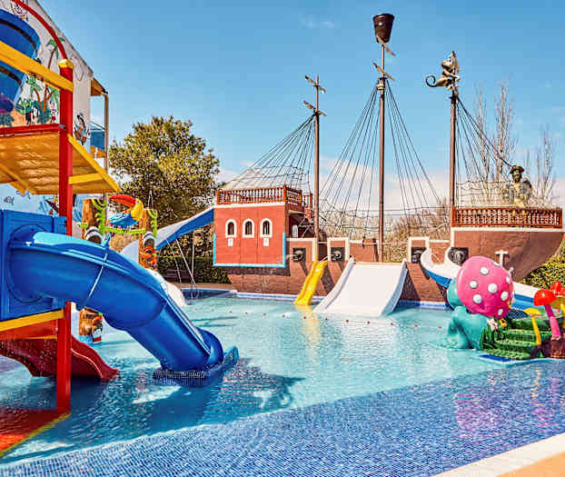 Bild av en vattenpark med ett pirattemat skepp, färgglada rutschkanor och lekskulpturer i en pool. (AI-genererad text)