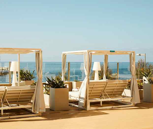 Två solsängar med vit takstruktur och gardiner på en terrass med havsutsikt. (AI-genererad text)