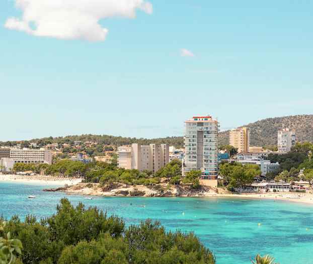 En kuststad med hotell byggnader vid en strand och klart turkost vatten. (AI-genererad text)
