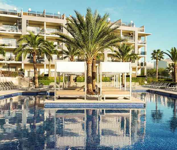 Bild av hotellpool med solstolar, palmer och byggnader i bakgrunden. (AI-genererad text)
