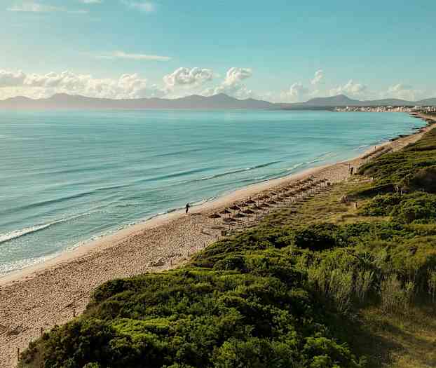 Strand med parasoller, hav och berg i bakgrunden. (AI-genererad text)