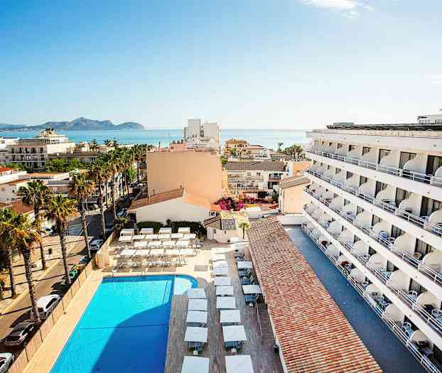 Vy från ovan över en hotellbyggnad, pool och omgivande område, med havet i bakgrunden. (AI-genererad text)