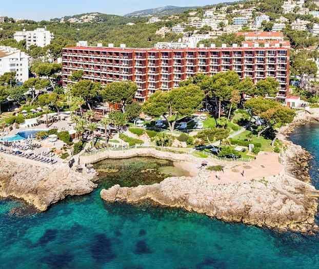 Flygfoto av en lyxresort vid havskusten med omgivande grönska och poolområden. (AI-genererad text)