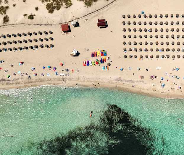 Luftvy över en strand med parasoller, människor och klart vatten. (AI-genererad text)