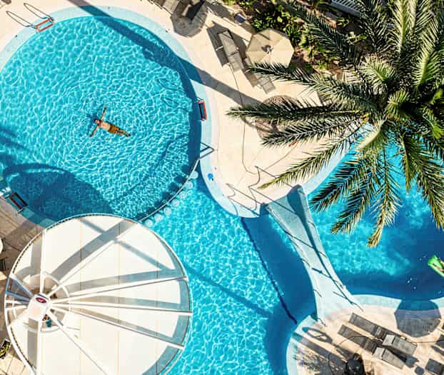 En utomhuspool omgiven av solstolar och parasoller, med en person som simmar. (AI-genererad text)