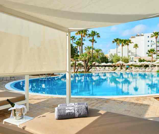 En lyxig cabana nära en pool med palmer och parasoller runt omkring. (AI-genererad text)