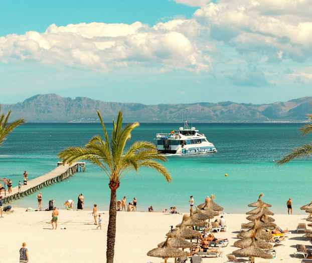 Strand med palmer och parasoller samt turister vid en brygga och en båt i havet. (AI-genererad text)