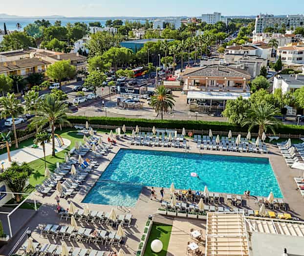 En pool omgärdad av solstolar, med omgivande grönska och byggnader i bakgrunden. (AI-genererad text)