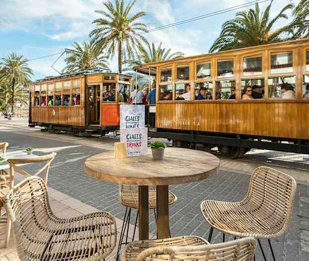 En träspårvagn passerar vid ett torg med bord och stolar. (AI-genererad text)
