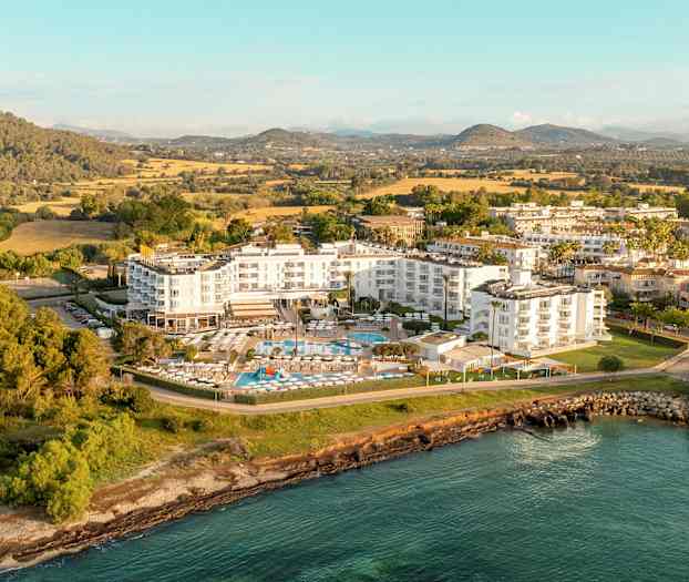 Flygbild över ett hotellkomplex omgivet av grönska och vattnet. (AI-genererad text)