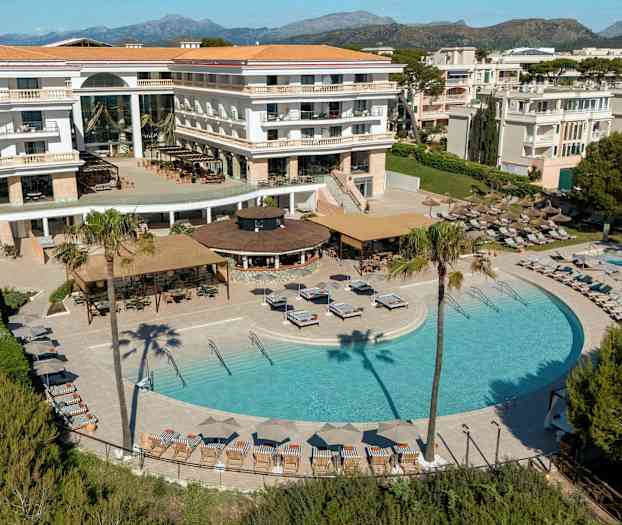 Hotell med pool- och terrassområde omgivet av solstolar, parasoller och grönska. (AI-genererad text)