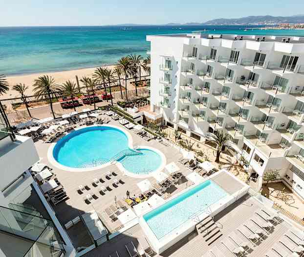 Hotellområde med pool och solstolar, strand och hav i bakgrunden. (AI-genererad text)