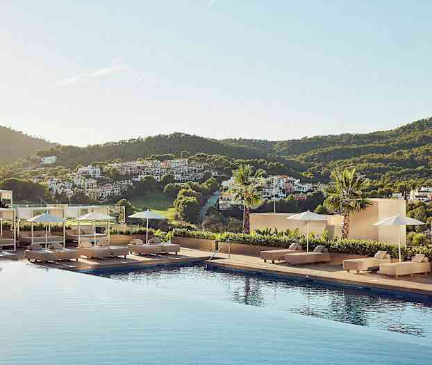 En utsikt från ett hotellområde med en pool omgiven av solstolar, parasoller och en grönskande landsbygd i bakgrunden. (AI-genererad text)