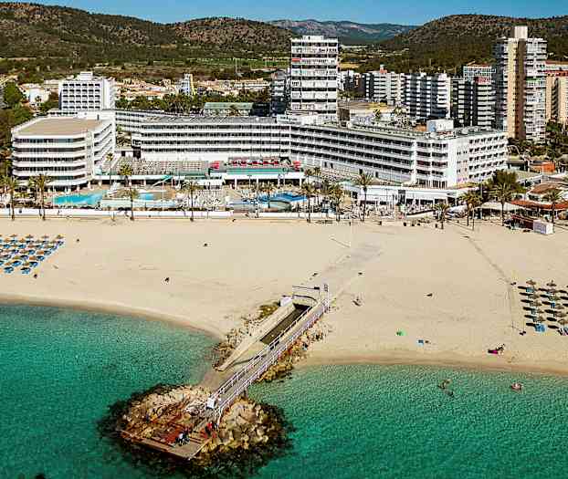Bild av en sandstrand med solstolar och parasoll, en brygga som leder ut i havet, och hotellbyggnader i bakgrunden. (AI-genererad text)