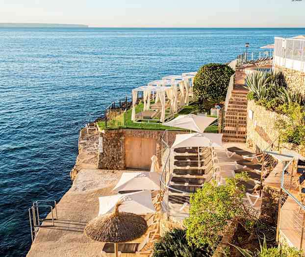 Utsikt över en klippavsats vid havet med solstolar, parasoll och grönområden. (AI-genererad text)