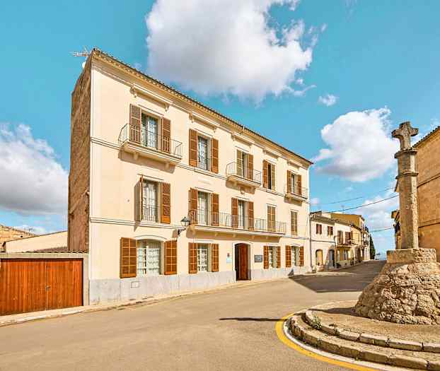 Gata med en byggnad med ljus fasad och en stenpelare med kors. (AI-genererad text)