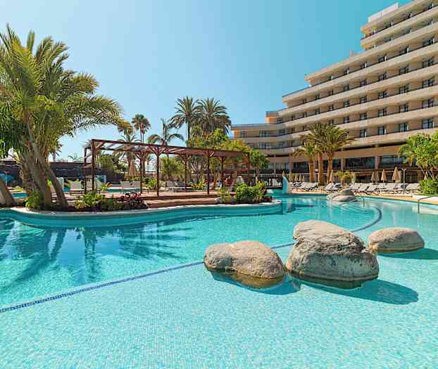 Utomhuspool med klart vatten, omgiven av palmer och solstolar framför en hotellbyggnad. (AI-genererad text)